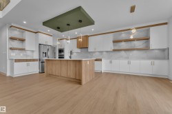 Light wood-finish flooring, white cabinetry with gold-toned hardware, center island with light countertop, built-in stainless steel appliances, and decorative suspended light fixtures - 