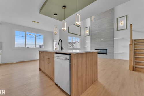 Kitchen island with wood-finish cabinetry and white countertop, integrated dishwasher, and black faucet - 764 Astoria Way, Devon, AB - Indoor Photo Showing Kitchen