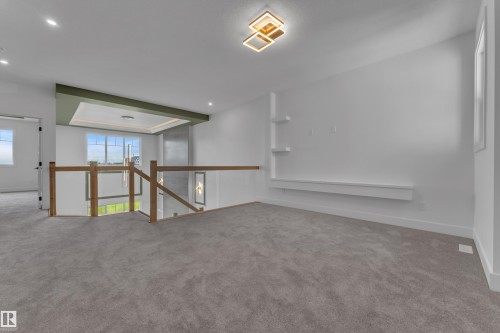 Carpeted loft space with a modern ceiling light fixture, built-in shelving, and a wood and glass railing - 764 Astoria Way, Devon, AB - Indoor Photo Showing Other Room