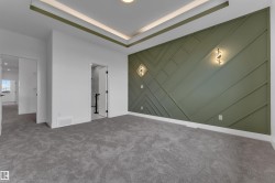 Recessed ceiling lighting, tray ceiling detail, feature wall with geometric paneling, decorative wall sconces, and neutral-toned carpeting - 