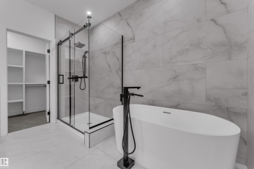 Freestanding soaking tub, walk-in shower with matte black fixtures, full-height wall tiling, and tile flooring - 764 Astoria Way, Devon, AB - Indoor Photo Showing Bathroom