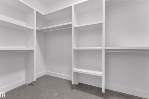 Custom closet system featuring white built-in shelving, multiple hanging rods, and gray carpet flooring - 764 Astoria Way, Devon, AB - Indoor With Storage