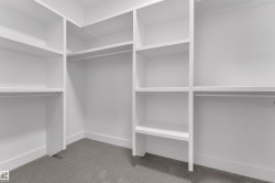 Custom closet system featuring white built-in shelving, multiple hanging rods, and gray carpet flooring - 