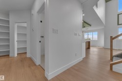 Light wood-finish flooring throughout, built-in shelving, white walls, and a staircase with a wood handrail - 