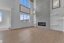 Expansive living space featuring wood-finish flooring, a tall ceiling, and abundant natural light from large windows - 