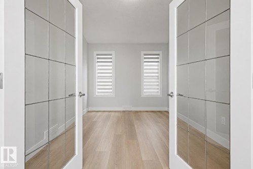 Double French doors with frosted glass panels, light wood-finish flooring, and two windows with blinds. Optional 5th bedroom! - 11816 168 Avenue Nw, Edmonton, AB - Indoor Photo Showing Other Room