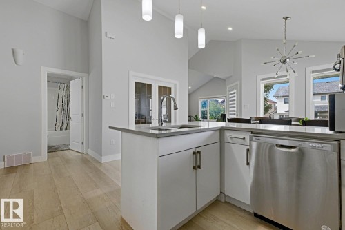 Vaulted ceilings, wood-finish flooring, white cabinetry, integrated stainless steel dishwasher, and a kitchen island with sink - 11816 168 Avenue Nw, Edmonton, AB - Indoor Photo Showing Kitchen With Upgraded Kitchen