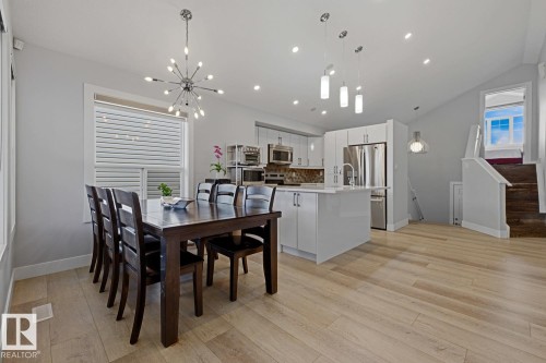 Light wood-finish flooring, recessed lighting, white kitchen cabinetry with stainless steel appliances, and a contemporary dining area chandelier - 11816 168 Avenue Nw, Edmonton, AB - Indoor