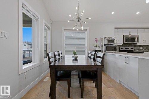 Light wood-finish flooring, contemporary chandelier, kitchen island with integrated cabinetry, stainless steel appliances, and a tiled backsplash - 11816 168 Avenue Nw, Edmonton, AB - Indoor