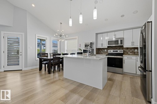 Open-concept kitchen and dining area featuring vaulted ceilings, wood-finish flooring, a kitchen island with pendant lighting, and stainless steel appliances - 11816 168 Avenue Nw, Edmonton, AB - Indoor Photo Showing Kitchen With Upgraded Kitchen