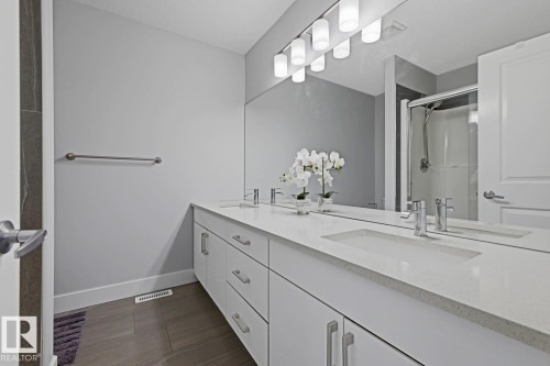 Double vanity with integrated sinks, polished chrome fixtures, white cabinetry, and wood-finish flooring - 11816 168 Avenue Nw, Edmonton, AB - Indoor Photo Showing Bathroom