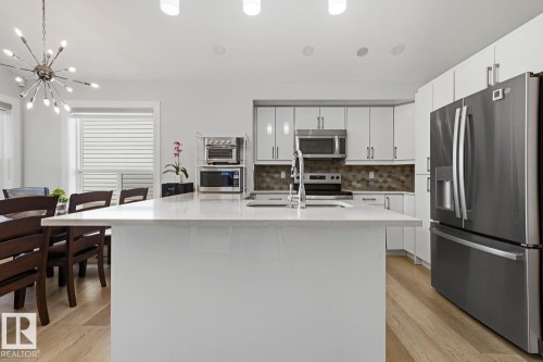 Kitchen featuring a white island with an integrated sink, stainless steel appliances, white cabinetry, and wood-finish flooring - 11816 168 Avenue Nw, Edmonton, AB - Indoor Photo Showing Kitchen With Double Sink With Upgraded Kitchen