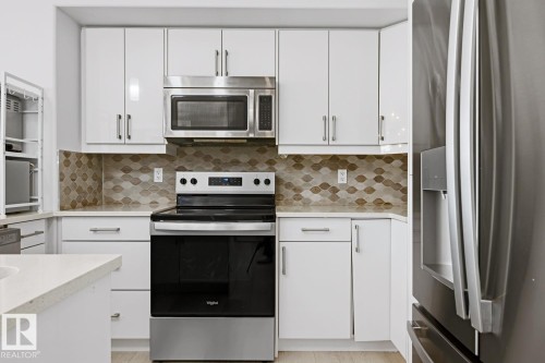 Glossy white cabinetry, geometric patterned backsplash, stainless steel appliances, white countertops, and wood-finish flooring - 11816 168 Avenue Nw, Edmonton, AB - Indoor Photo Showing Kitchen With Upgraded Kitchen