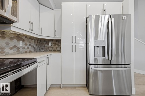 Sleek kitchen featuring white high-gloss cabinetry, stainless steel appliances, a mosaic tile backsplash, and light-toned countertops - 11816 168 Avenue Nw, Edmonton, AB - Indoor Photo Showing Kitchen With Upgraded Kitchen