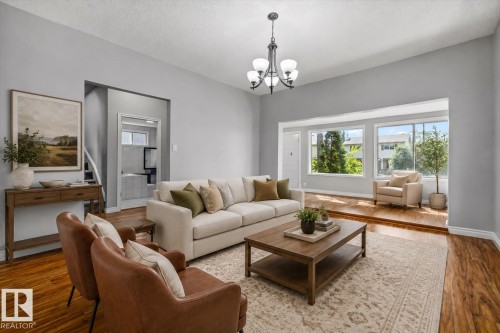 Spacious living area featuring wood-finish flooring, a contemporary chandelier, large windows, and an arched entry - 11429 64 Street Nw, Edmonton, AB - Indoor Photo Showing Living Room