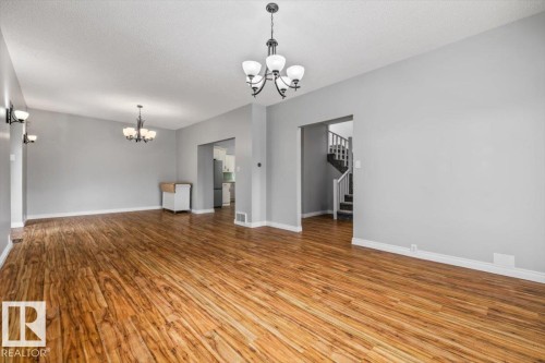 Open concept main level featuring wood-finish flooring, light grey painted walls, and multiple chandeliers - 11429 64 Street Nw, Edmonton, AB - Indoor Photo Showing Other Room