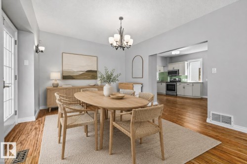 Recessed kitchen opening, wood-finish flooring, wall sconce lighting, and a contemporary chandelier - 11429 64 Street Nw, Edmonton, AB - Indoor Photo Showing Dining Room