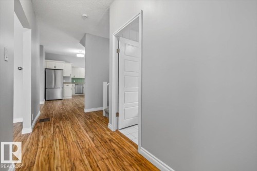 Wood-finish flooring throughout, bright white trim, and a modern interior door with panel detailing - 11429 64 Street Nw, Edmonton, AB - Indoor