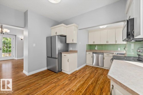 Wood-finish flooring, white cabinetry, stainless steel appliances, green tile backsplash, and light-toned countertops - 11429 64 Street Nw, Edmonton, AB - Indoor Photo Showing Kitchen With Stainless Steel Kitchen