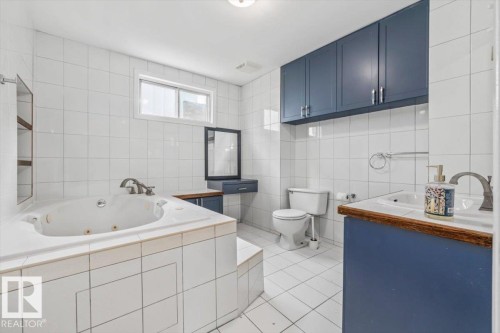 White tiled walls and flooring with a jetted soaking tub - 11429 64 Street Nw, Edmonton, AB - Indoor Photo Showing Bathroom