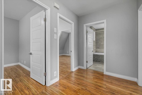 Wood-finish flooring throughout, modern interior doors with brushed nickel hardware, light gray wall finish, and a bathroom featuring stone tile walls and a mosaic-tiled tub surround - 11429 64 Street Nw, Edmonton, AB - Indoor Photo Showing Other Room