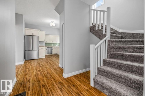 Curved staircase with carpeted treads, white railing, wood-finish flooring, and a kitchen featuring light-toned cabinetry and stainless steel appliances - 11429 64 Street Nw, Edmonton, AB - Indoor