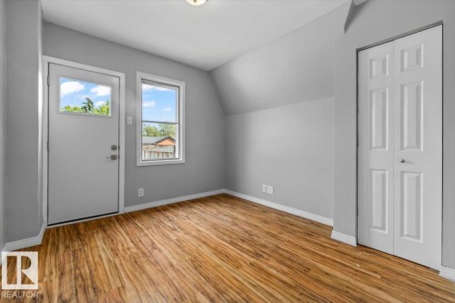 Wood-finish flooring, light gray wall paint, a white door with an integrated window, a white-framed window, and white bi-fold closet doors - 11429 64 Street Nw, Edmonton, AB - Indoor Photo Showing Other Room