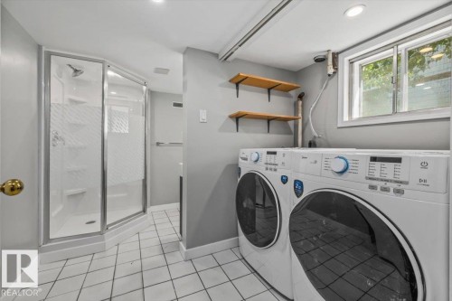 White tiled flooring, recessed lighting, built-in shower with glass enclosure, dual laundry appliances, and two wall-mounted wooden shelves - 11429 64 Street Nw, Edmonton, AB - Indoor Photo Showing Laundry Room