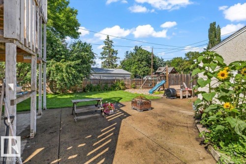 Expansive concrete patio with a fire pit, bordered by a manicured lawn and mature trees - 11429 64 Street Nw, Edmonton, AB - Outdoor
