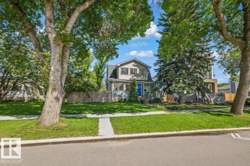 Gabled roofline with dormer windows, stone facade, covered front porch, and mature trees framing the property - 11429 64 Street Nw, Edmonton, AB - Outdoor