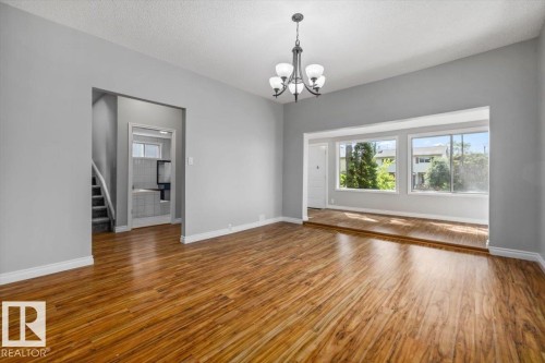 Wood-finish flooring throughout, with a classic chandelier fixture, and a spacious window area providing ample natural light - 11429 64 Street Nw, Edmonton, AB - Indoor