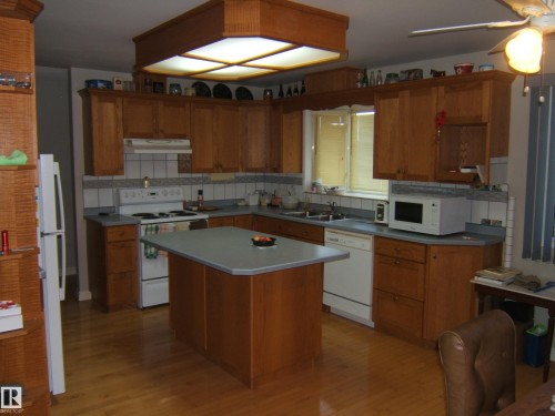 Kitchen with wood-finish cabinetry, central island, light-toned countertops, and wood-finish flooring - 5404 49 Street, Two Hills, AB - Indoor Photo Showing Kitchen With Double Sink