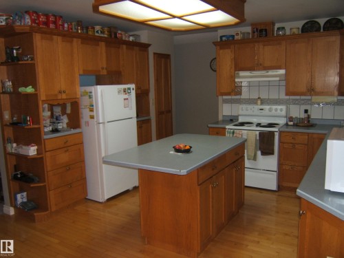 Kitchen featuring wood-finish cabinetry, a central island with a grey countertop, white appliances, and wood-finish flooring - 5404 49 Street, Two Hills, AB - Indoor Photo Showing Kitchen