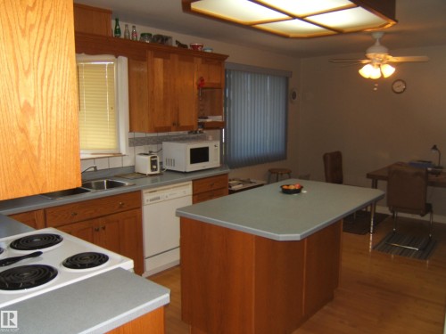 Kitchen featuring wood-finish cabinetry, a built-in dishwasher, a double basin sink, an electric range, and a ceiling fan - 5404 49 Street, Two Hills, AB - Indoor Photo Showing Kitchen With Double Sink