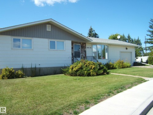 Ranch-style exterior with white siding, stone façade detailing, a single-car garage, multiple pane windows, and a landscaped front yard with a concrete walkway - 5404 49 Street, Two Hills, AB - Outdoor