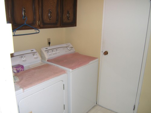 Built-in wood cabinetry, light-toned wall paint, and a white door with a brass-toned knob - 5404 49 Street, Two Hills, AB - Indoor Photo Showing Laundry Room