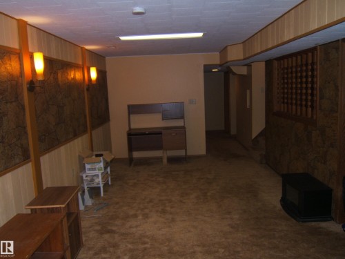 Wall paneling featuring a stone-look texture and wood-finish trim, plush carpet flooring, and a drop ceiling - 5404 49 Street, Two Hills, AB - Indoor Photo Showing Other Room