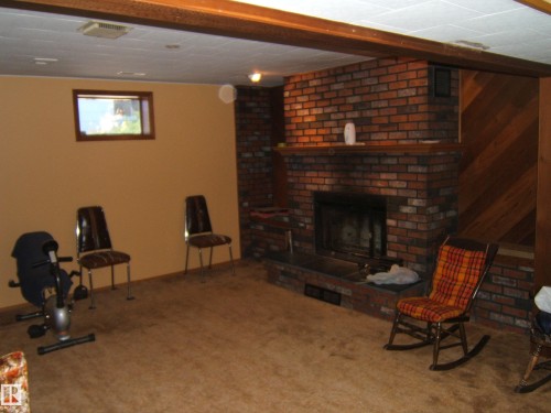Brick fireplace with hearth, wood-finish mantel, and diagonal wood-paneled accent wall - 5404 49 Street, Two Hills, AB - Indoor With Fireplace