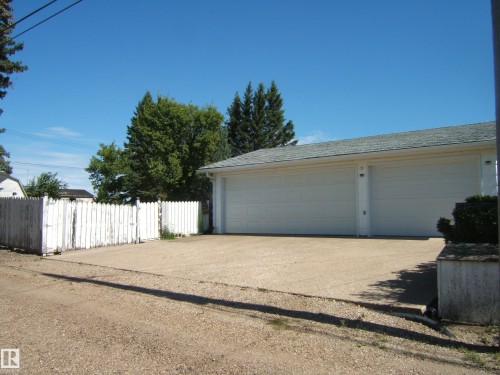 Detached two-car garage with white overhead doors, shingle roofing, and a gravel driveway - 5404 49 Street, Two Hills, AB - Outdoor