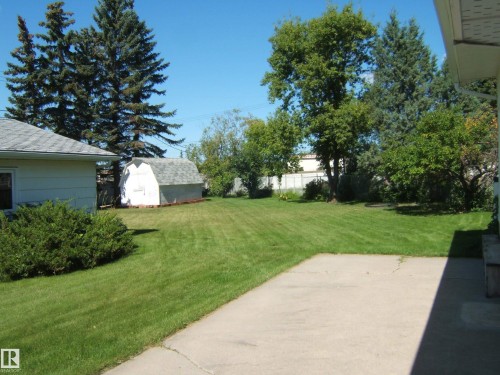 Expansive grass lawn featuring a concrete patio, mature trees, and a storage shed with a shingled roof - 5404 49 Street, Two Hills, AB - Outdoor