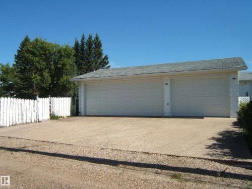 Two-car garage with individual white doors, concrete driveway, and gray shingle roof - 5404 49 Street, Two Hills, AB - Outdoor
