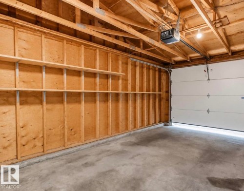 Garage interior featuring exposed wood framing, built-in shelving, concrete flooring, and an overhead garage door opener mechanism - 3221 132A Avenue Nw, Edmonton, AB - Indoor Photo Showing Garage