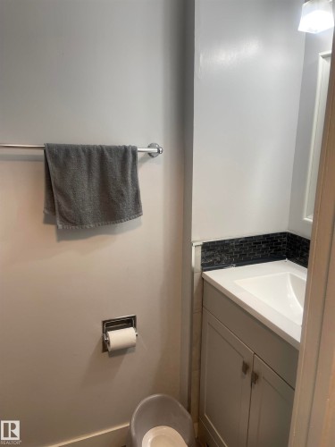 Bathroom vanity featuring a white rectangular sink, light gray cabinetry with brushed nickel hardware, and a dark mosaic tile backsplash - 3221 132A Avenue Nw, Edmonton, AB - Indoor Photo Showing Bathroom