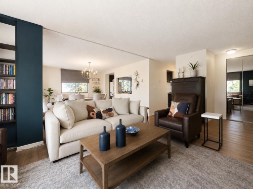 Open-concept living area with wood-finish flooring, a built-in bookshelf, and a dining area featuring a chandelier - #301 9808 103 St Nw, Edmonton, AB - Indoor Photo Showing Living Room