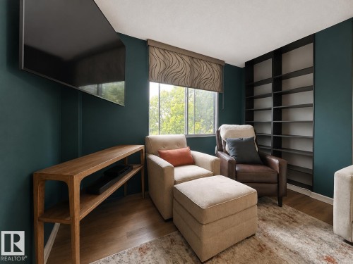 Room featuring a large window with a patterned roller shade, built-in shelving, a wall-mounted television, and wood-finish flooring - #301 9808 103 St Nw, Edmonton, AB - Indoor