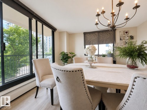 Dining area featuring expansive floor-to-ceiling windows with roller shades, light wood-finish flooring, and a multi-arm chandelier - #301 9808 103 St Nw, Edmonton, AB - Indoor Photo Showing Dining Room