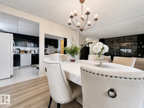 Open-concept dining area featuring a bronze chandelier and wood-finish flooring - #301 9808 103 St Nw, Edmonton, AB - Indoor Photo Showing Dining Room