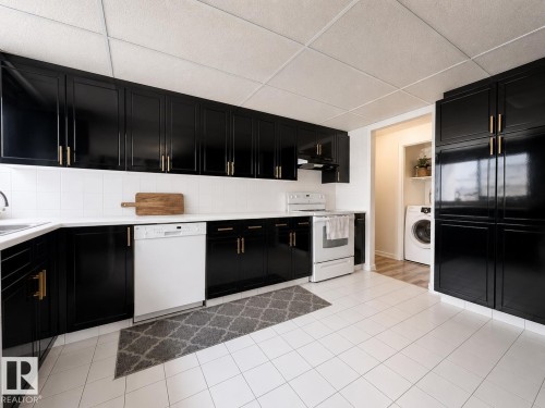 Kitchen featuring black cabinetry with gold hardware, white tile backsplash, white countertops, and white tile flooring - #301 9808 103 St Nw, Edmonton, AB - Indoor Photo Showing Kitchen