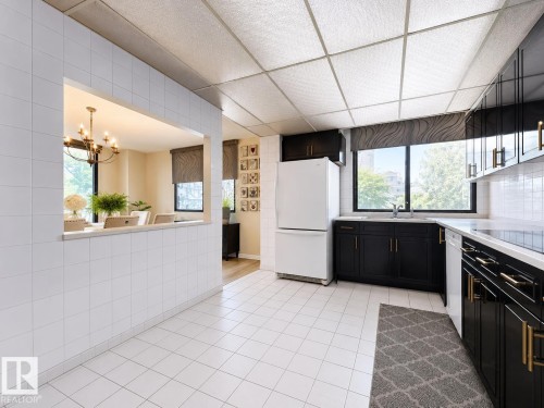 Bright kitchen featuring white tile flooring, black cabinetry with gold-tone hardware, white countertops, and a pass-through opening to an adjacent room - #301 9808 103 St Nw, Edmonton, AB - Indoor Photo Showing Kitchen