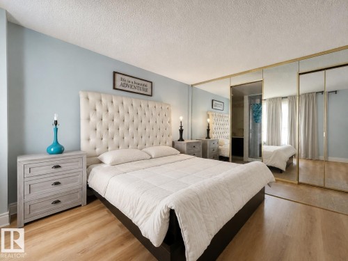 Light wood-finish flooring complements the tufted headboard - #301 9808 103 St Nw, Edmonton, AB - Indoor Photo Showing Bedroom